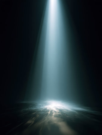 A light beam source shines brightly in darkness, casting a strong glow on the surface below, creating striking contrast and depth.の素材