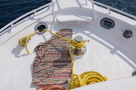 Colorful woven rug placed on the deck of a boat, surrounded by yellow ropes and blue water, illuminated by bright sunlightの写真素材