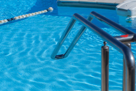Swimming pool features clear blue water and a stainless steel ladder, with sunlight creating...
