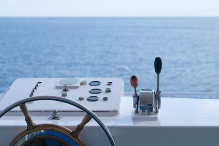 Boat steering wheel and control panel featuring throttle lever, with a clear view of calm ocean waters under bright daylightの写真素材