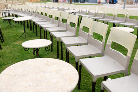 Gray plastic chairs and round tables are neatly arranged on green grass in an outdoor area, suitable...