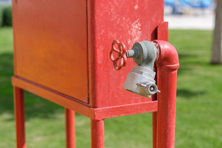 Red fire hydrant featuring a valve and pipe, situated on a green lawn outdoors, with a clear blue...