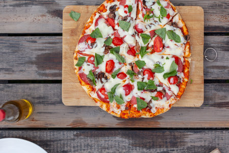 Freshly baked pizza topped with mozzarella cheese, cherry tomatoes, and basil leaves on a wooden cutting board with rustic background