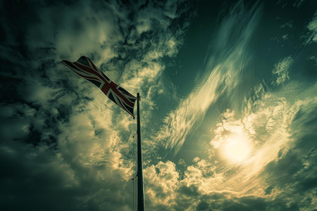 Silhouetted uk flag waving in the wind with a backdrop of a moody, sunlit skyの素材