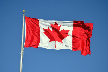 Vibrant canadian flag flutters in the breeze, set against a clear blue backdropの素材