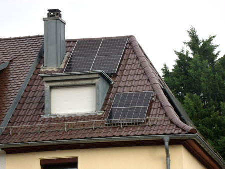 A private house is equipped with several solar panels mounted on a sloped tiled roof to generate eco-friendly electricity.の写真素材