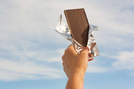 Hands of a woman holding a tile of chocolate against the skyの写真素材