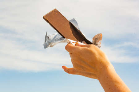 Hands of a woman holding a tile of chocolate against the skyの写真素材