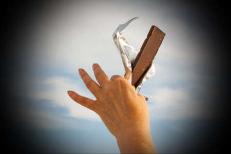 Hands of a woman holding a tile of chocolate against the skyの写真素材