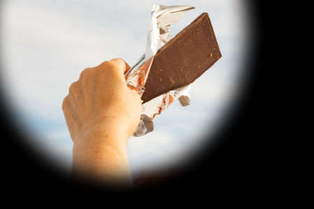 Hands of a woman holding a tile of chocolate against the skyの写真素材