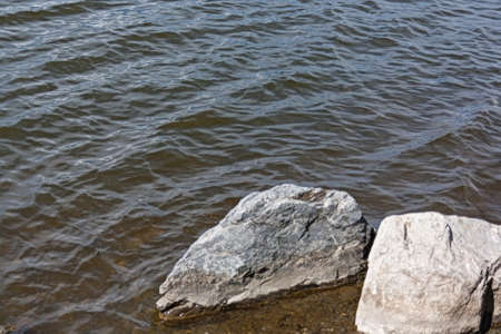 Large rocks near the shore washed by the waves of the lake sunny summer dayの写真素材