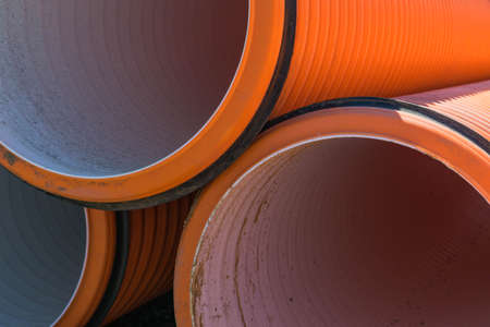 Pipes of PVC large diameter orange color prepared for laying on construction siteの写真素材