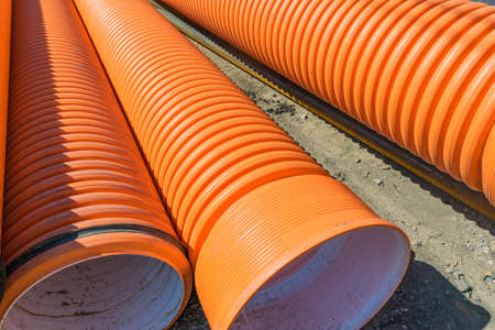 Pipes of PVC large diameter orange color prepared for laying on construction siteの写真素材