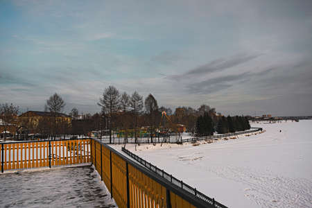 Winter landscape with snowy field, leafless trees and frozen lake in city park.