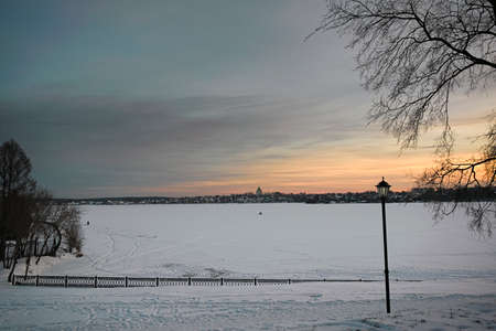 Winter landscape with snowy field, leafless trees and frozen lake in city park.の写真素材
