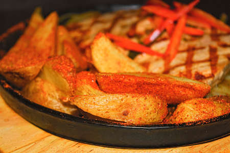 Pork steak with fried potatoes and onions on a cast-iron brazierの写真素材