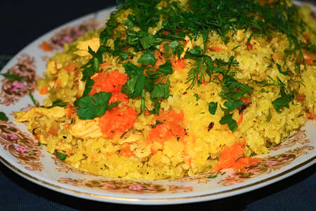 pilaf with meat with greens on a white plate.