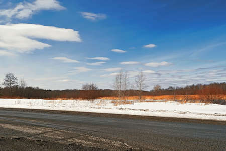 Rural road through a field of melting snow in early springの写真素材