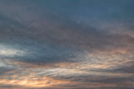 feathery clouds in the blue sky are illuminated by the rays of the sun, setting over the horizon