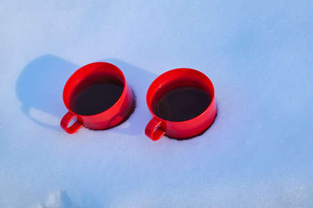 Two red cups of hot tea stand in the snow close-up