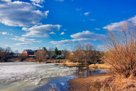 Spring landscape melts ice on a small river at the edge of the village.の写真素材