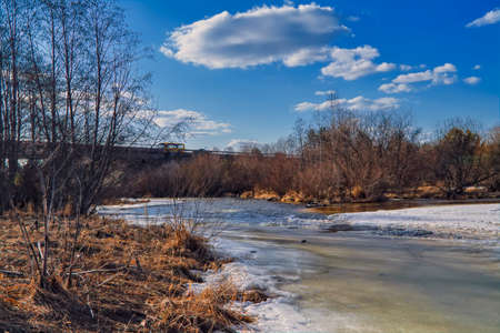 Spring landscape melts ice on a small river at the edge of the village.