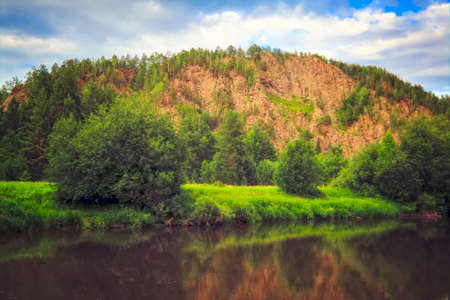 Summer landscape river with reflecting trees against the backdrop of forests and mountains. On a...