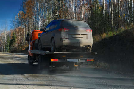 Tow truck rides along a forest road against the backdrop of an autumn forest. Help on road...