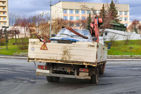 A car tow truck transports a damaged car through the city streets.