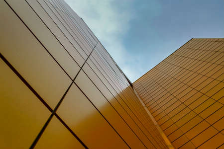 Wall of a high-rise building faced with yellow tiles against the sky. Bottom view.の写真素材