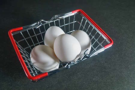 White chicken eggs in a metal grocery basket on a dark background.
