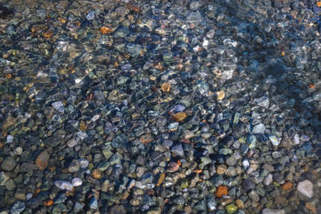 Closeup of a water surface with pebbles at the bottom of a small stream with transparent clear water. Pebbles at the bottom of a small stream in nature.の写真素材