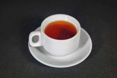 White cup with black tea on a white saucer on a dark background. A cup of tea in saucer on top of dark textured table.の写真素材
