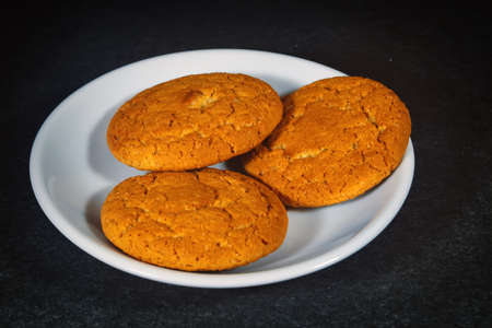 Oatmeal cookies on a white porcelain saucer on a dark background close-up.