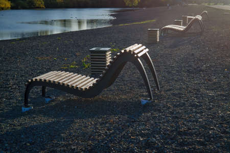 Wooden benches on the river bank in a city park in the light of the setting sun. Autumn landscape.