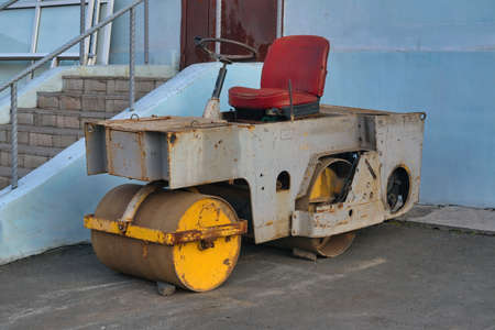 A small asphalt roller stands at the front porch of the building. Side view.