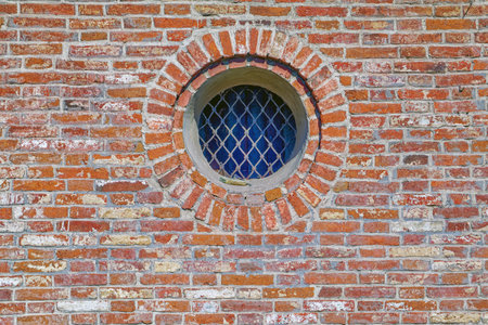 The red brick wall with the small round window. Fragment of an old red brick wall with a round...