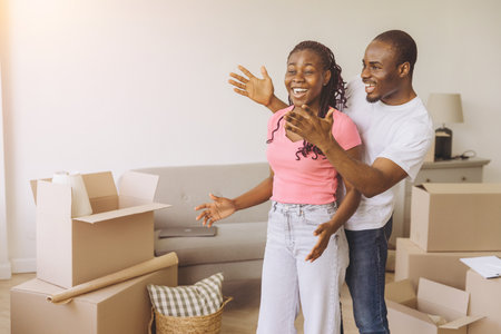 African American Man covering woman's eyes, making a surprise in their new apartment, surrounded by cardboard boxesの写真素材