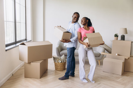 Smiling couple carrying cardboard boxes, joyfully moving into their new home, embracing the excitement of fresh beginnings togetherの写真素材