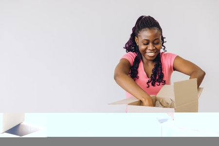 Happy African American woman unpacking belongings from cardboard box after moving into new house