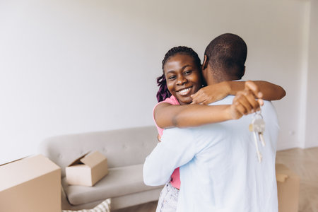 Young African American couple hugging joyfully while holding keys to their new home, celebrating a fresh start and exciting future togetherの写真素材