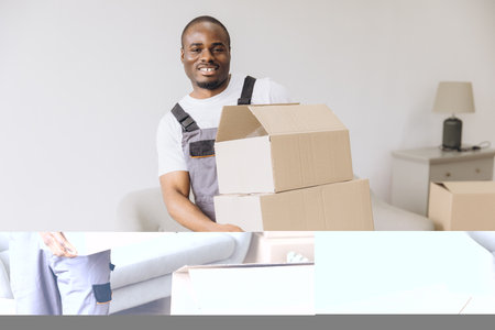 Smiling african american delivery man carrying cardboard boxes into new apartment during relocationの写真素材