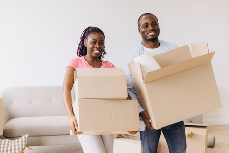 Smiling African American couple carrying cardboard boxes while moving into their new home, embracing the excitement of fresh beginningsの写真素材