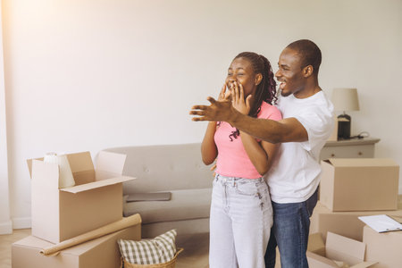 African American Man covering woman's eyes, making a surprise in their new apartment, surrounded by cardboard boxesの写真素材