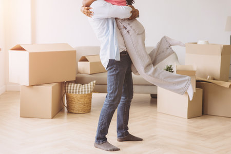 Young african american couple embracing each other while moving in new house, surrounded by cardboard boxesの写真素材