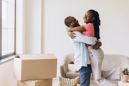 Young African American couple embracing while settling into their new apartment, surrounded by boxes and filled with excitement for their futureの写真素材