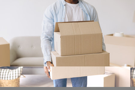 African American Man carrying two cardboard boxes is moving into a new home, surrounded by the excitement and challenges of starting fresh in a new spaceの写真素材