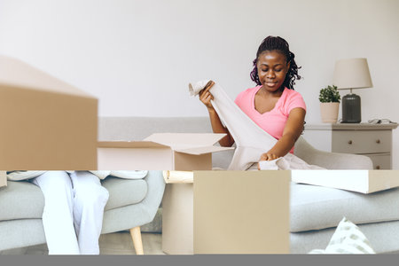 Happy african american homeowner unpacking boxes in a cozy living room, joyfully organizing belongings after moving into a new apartmentの写真素材