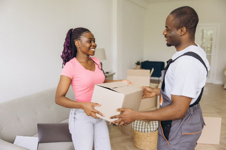 Professional African American movers assisting a homeowner with a cardboard box, ensuring a smooth and efficient moving processの写真素材