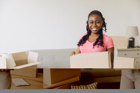 Happy african american woman moving home carrying cardboard box smiling unpacking belongings in new house real estate purchase property ownershipの写真素材